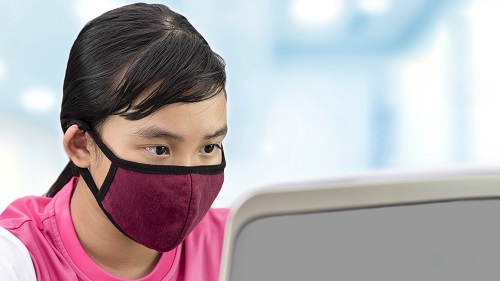 A girl wearing a mask looking at a laptop screen