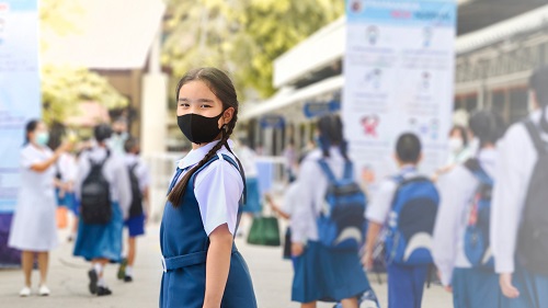 A girl wearing a uniform and mask looking at a camera at school