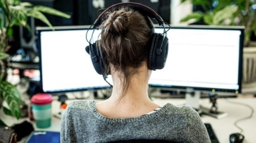 Woman at desk with two screens and headphones