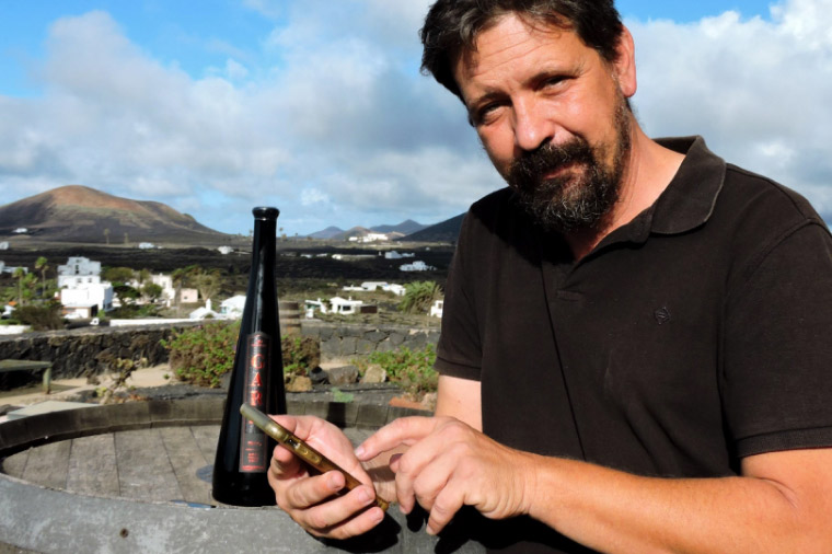 Winemaker poses with wine bottle in front of vineyard