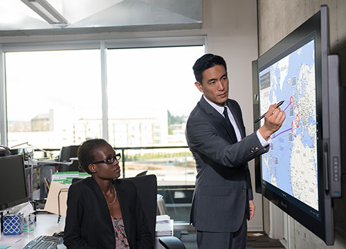 Homem apontando para o Surface Hub, para onde a mulher olha