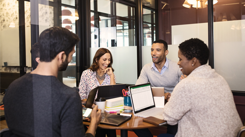 Das Bild zeigt eine Gruppe von Menschen um einen Tisch mit Surface Geräten vor ihnen.