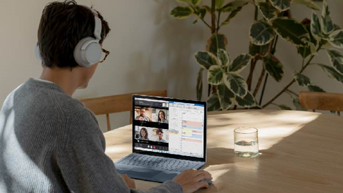 Das Bild zeigt einen Mann vor einem Surface Gerät, der Surface Headphones trägt und an einem Teamscall teilnimmt.