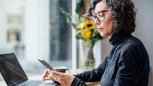 Das Bild zeigt eine Frau in einem Kaffee vor einem Surface Gerät, die parallel in ihr Smartphone schaut.