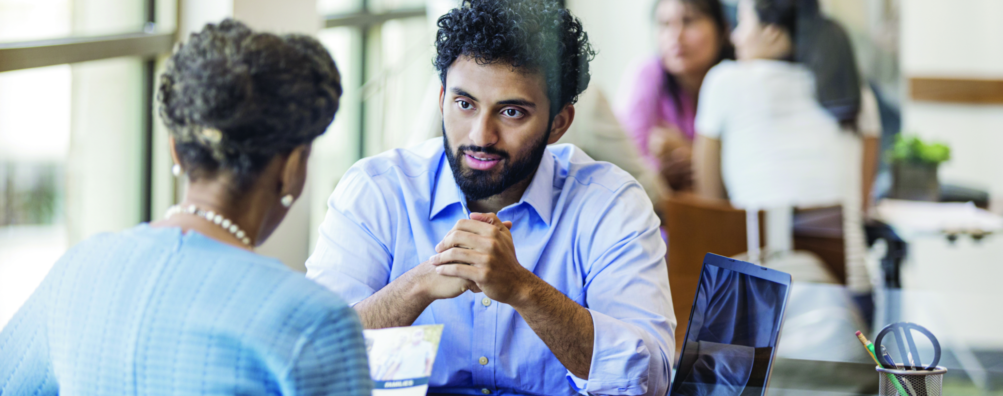 Two professionals discussing documents at a table with a laptop during a business meeting.