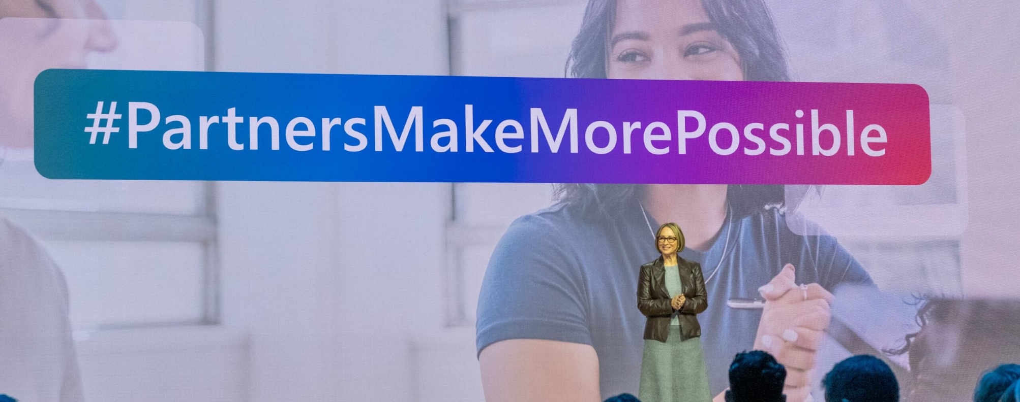 Nicole Dezen speaking in front of a screen which reads #PartnersMakeMorePossible