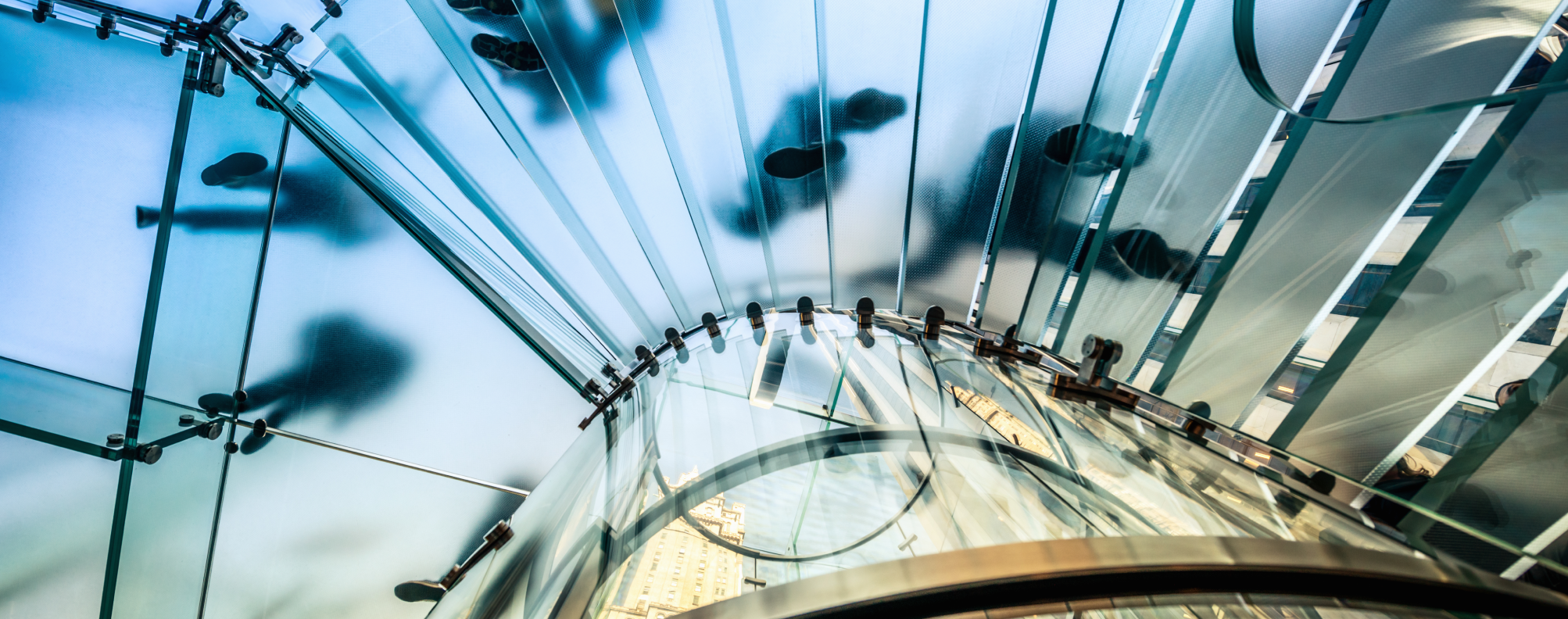 A view from below of people walking on a modern glass spiral staircase in a city building.