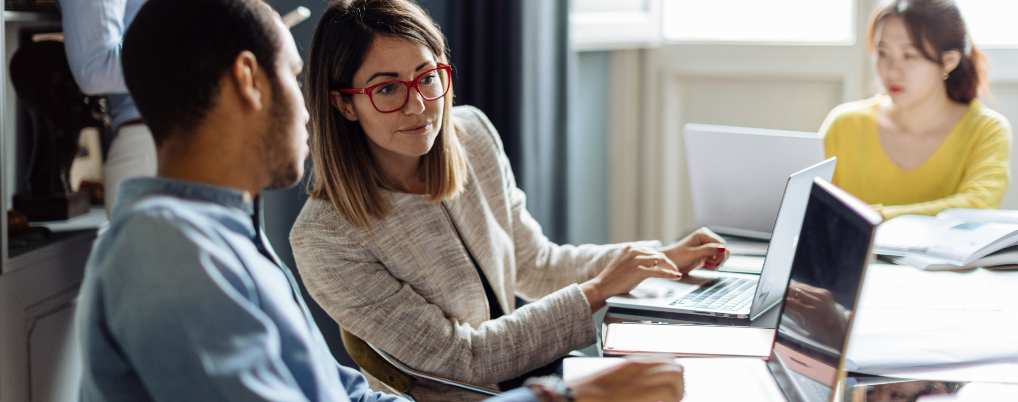 Two people at a conference room table looking at a laptop screen together.