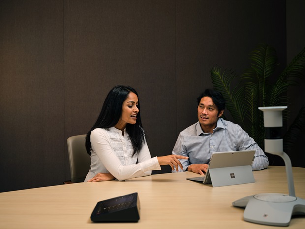 Two employees in a conference looking a shared Microsoft Surface laptop