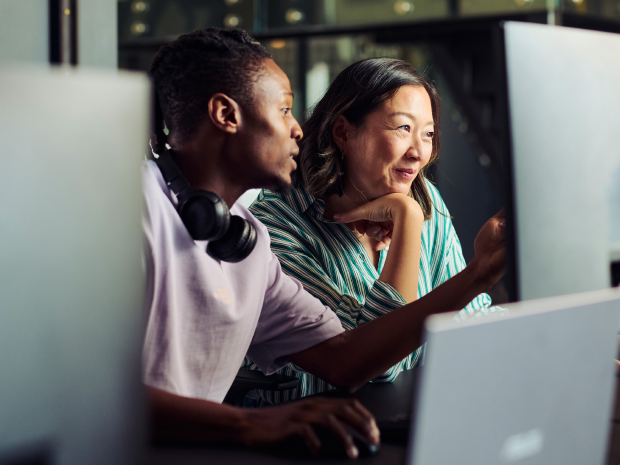 Two professionals collaborating at a desk, focused on a computer screen in a modern office setting.