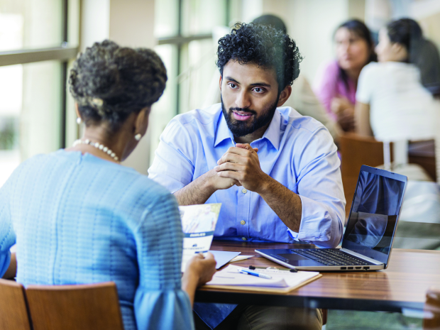Two professionals discussing documents at a table with a laptop during a business meeting.