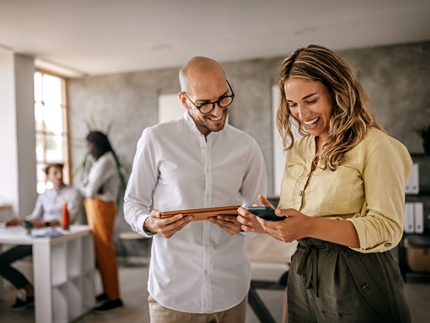 Cheerful female businesswoman standing with colleague looking at a digital tablet in a modern office space. 