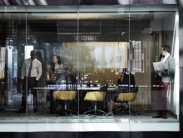 Outside view of five professional colleagues meeting in a glass-walled conference room