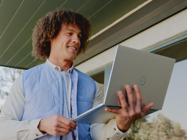 Man smiling as he walks outside holding a laptop