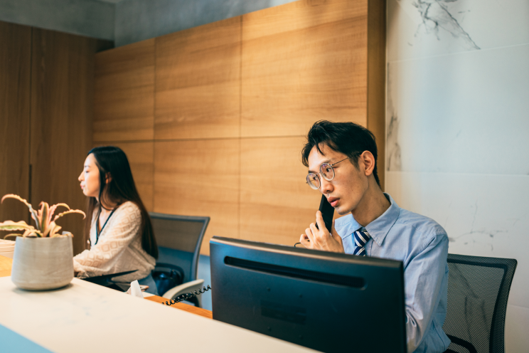 Two people working at a front desk one on the phone.