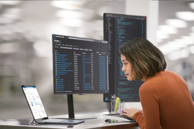A person in an office reviewing data across three monitors