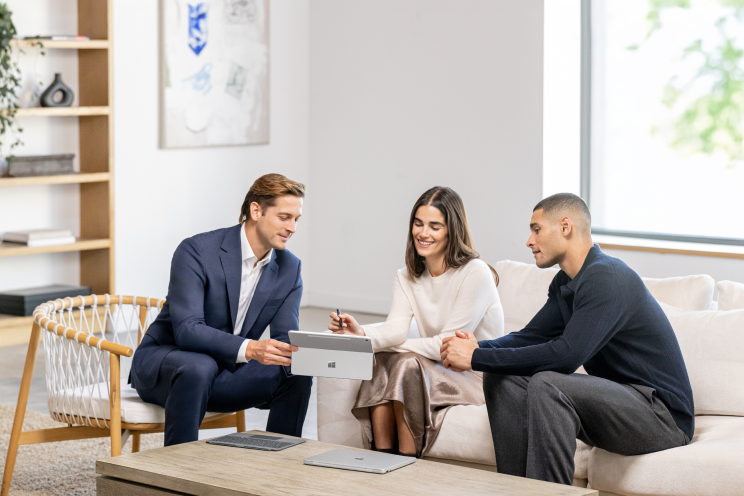 Three people seated, looking at a tablet.