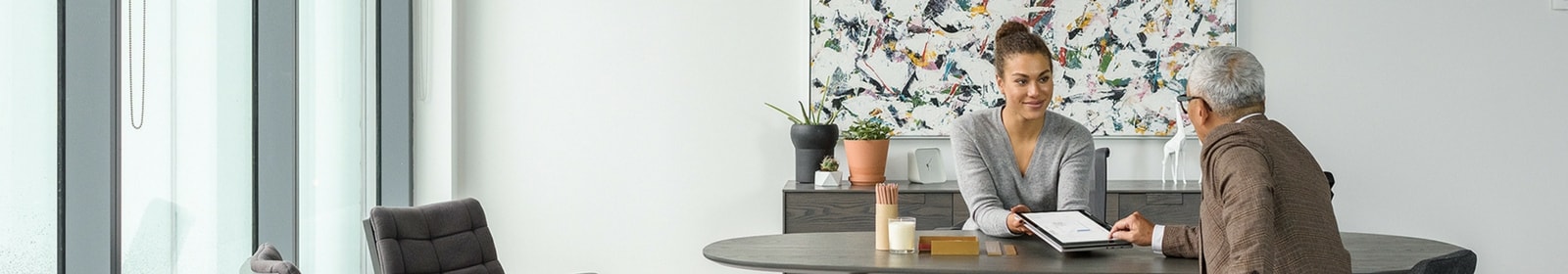 A woman shares information with a man on her tablet in her office