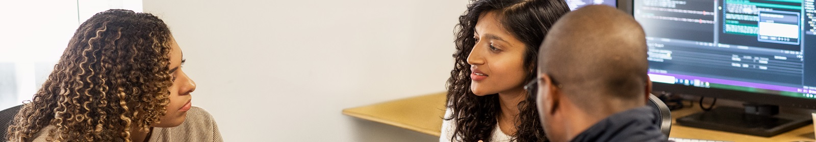 Three coworkers turned away from their workstations, meeting intently