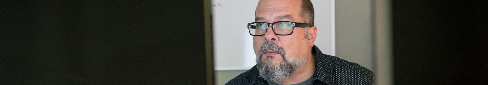 A bearded man scrutinizes files on two computers