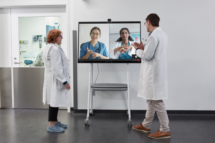 Two healthcare workers speaking with others on a big screen