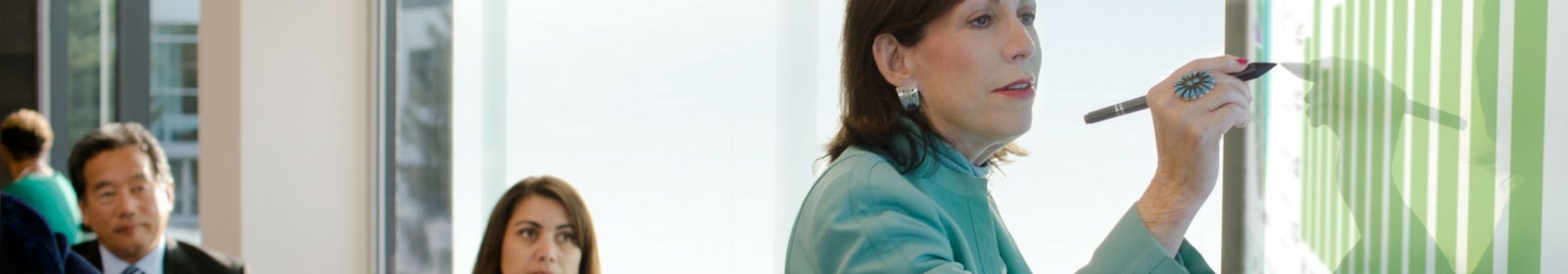 Person writes on whiteboard as colleagues observe.