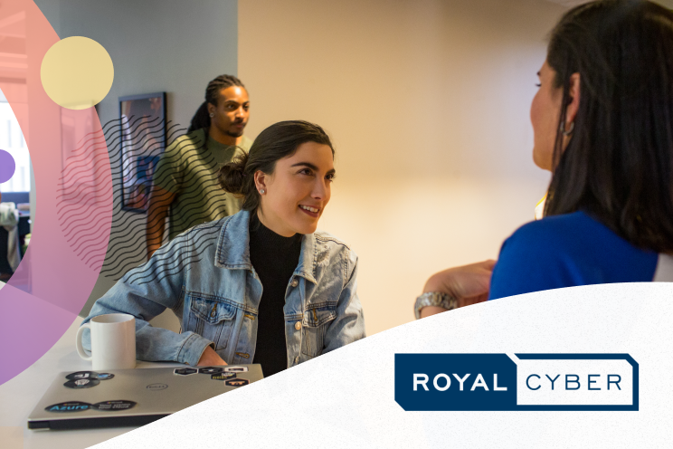 Two people talking in an office setting as another walks by.
