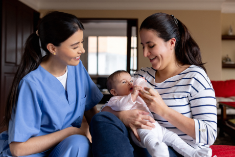 A person giving a bottle to a baby supervised by a nurse.