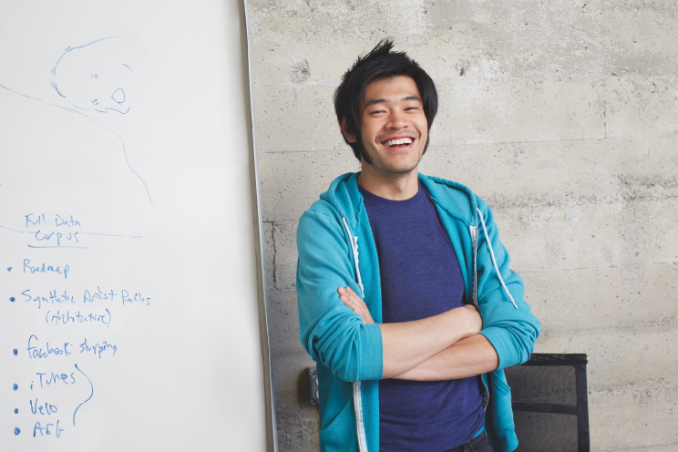 A smiling person standing in front of a white board.