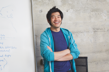 A smiling person standing in front of a white board.