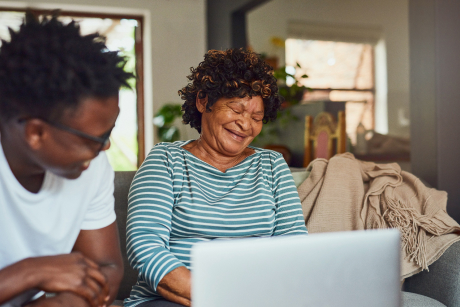 Two people laughing and sitting in front of a laptop