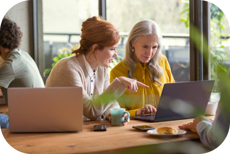 Two people seated in a cafeteria looking at a laptop.