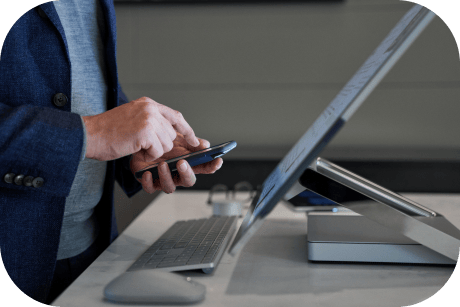 A persons hands using a smart phone in front of a computer