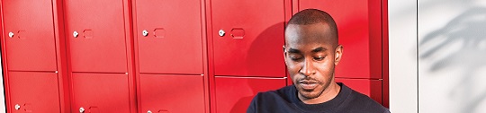 A man uses his tablet by a row of lockers