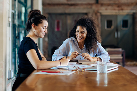 Two businesswomen work at a conference table.