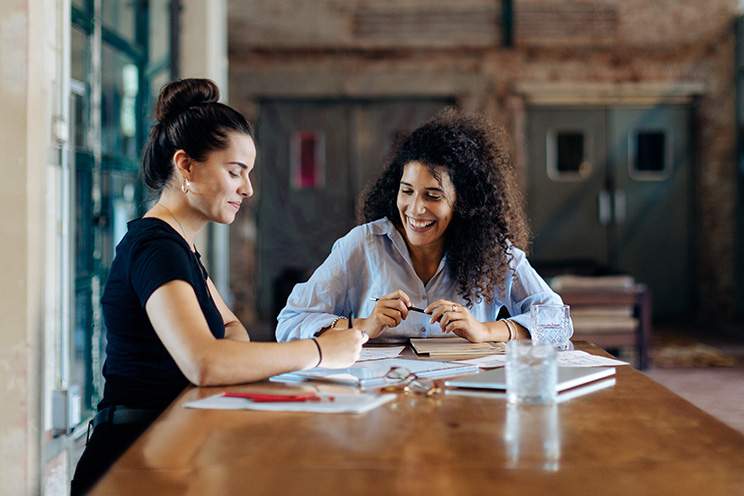 Two businesswomen work at a conference table.
