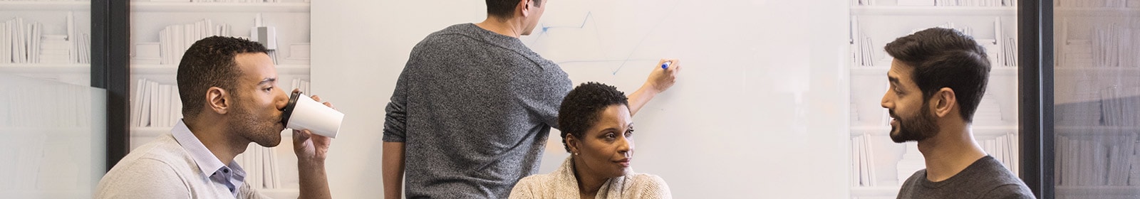 Coworkers having meeting at table with whiteboard behind them