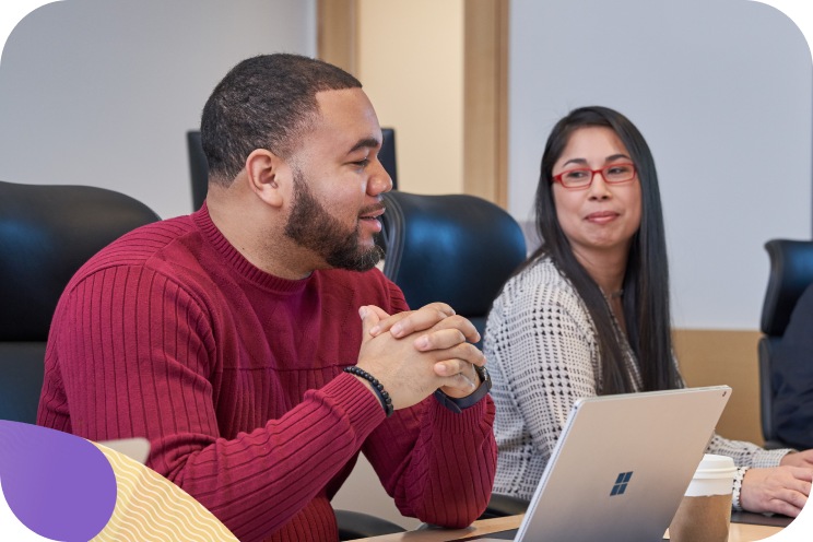 Two people sit at a shared workspace with one laptop