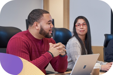 Two people sit at a shared workspace with one laptop