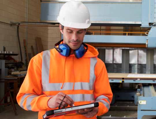 Man in orange jacket and white helmet looking at a computer tablet