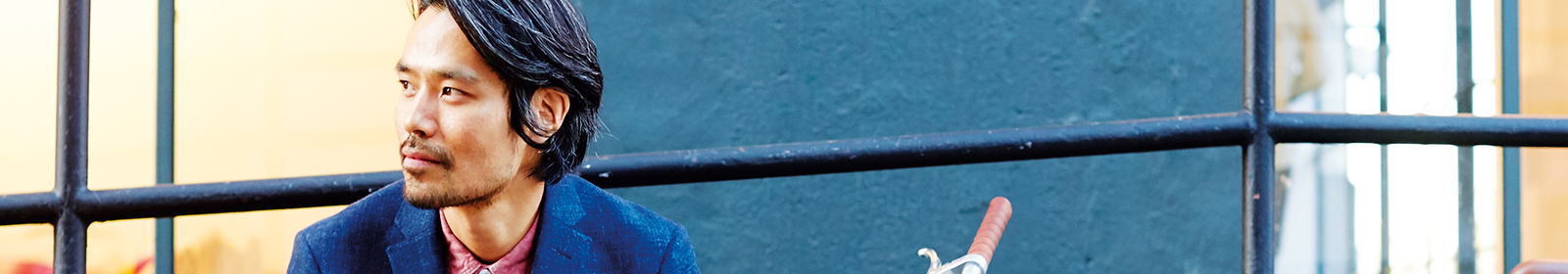Man with blue jacket and pink shirt in front of a blue wall