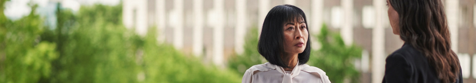 Two people talk outside, near a railing 
