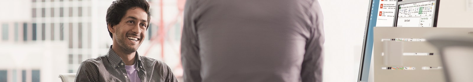 Man next to desktop monitor smiles at standing co-worker