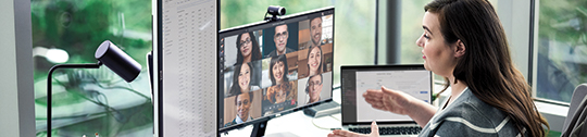 A seated woman gestures to a monitor with people in a Teams meeting