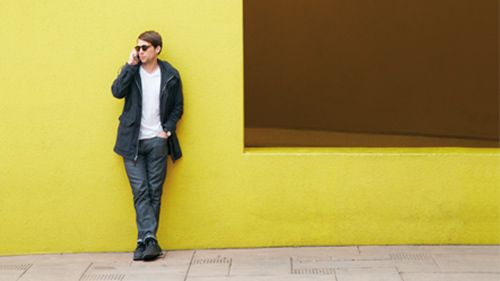 Man leaning against wall outside while talking on cell phone