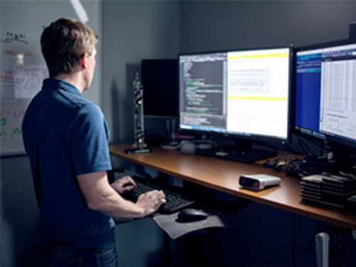 Male developer standing in front of monitors coding