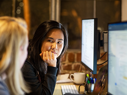 Two women having a discussion in front of their monitors