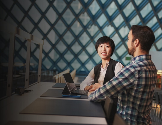 Woman and man sitting at a desk having a conversation in the Public Library with Surface Pro 4
