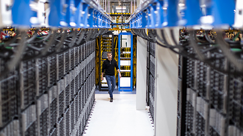 Un hombre caminando por un pasillo de servidores