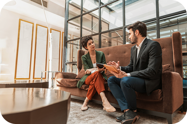 Two people sit on a couch discussing work.